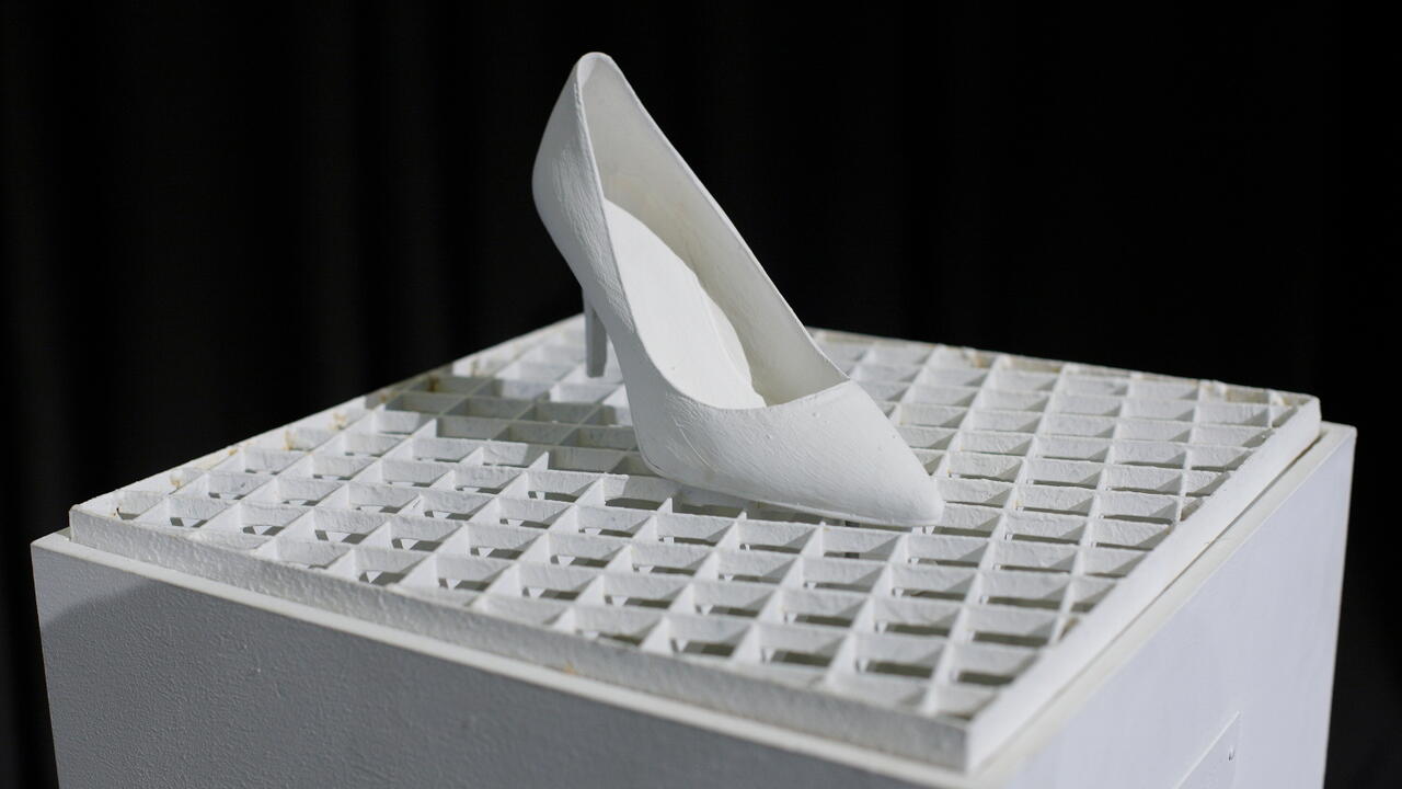 Wandern: Damenschuh mit sehr hohem Absatz auf einem um 15° nach rechts gedrehten Gitterrost. 